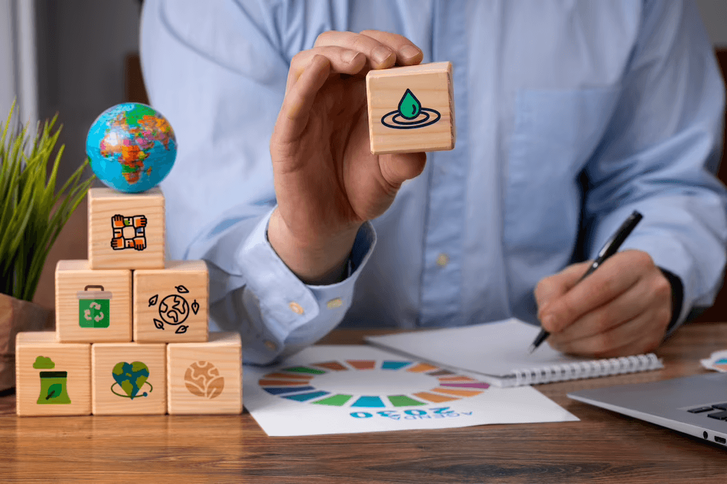 Uma pessoa segura um cubo de madeira com um desenho de gota d'água na face, com a outra mão escreve em uma folha de papel ao lado do logotipo da Agenda 2030